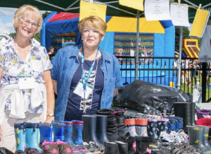 Deux femmes souriantes devant un kiosque présentant des articles usagés destinés à la vente, lors du Festival Lorettain.