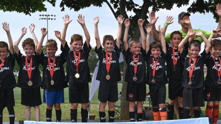 Groupe de petits garçons vêtus d'un uniforme de soccer sur un podium, tous les bras dans les airs. Ils portent tous une médaille dans le cou.