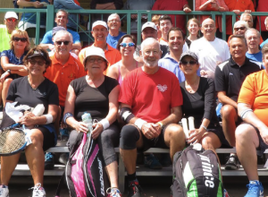Groupe de personnes tenant dans leurs mains une raquette de tennis, tous assis sur une estrade de métal et faisant face à la caméra.