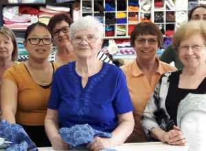 Femmes souriantes rassemblées devant un mur de rangement pleins de tissus.
