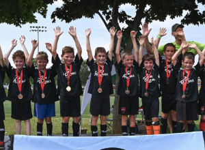 Groupe de petits garçons vêtus d'un uniforme de soccer sur un podium, tous les bras dans les airs. Ils portent tous une médaille dans le cou.