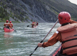 3 canots sur une rivière, aux côtés d'une montagne.