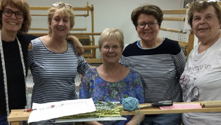 Groupe de femmes souriantes réunies devant des machines à tisser.